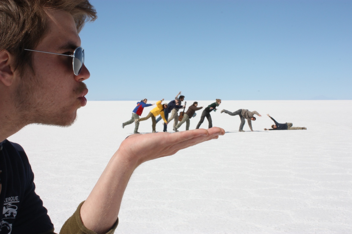 Forced-perspective photograph on the Uyuni salt flat: a person appears to hold tiny people on an outstretched hand.